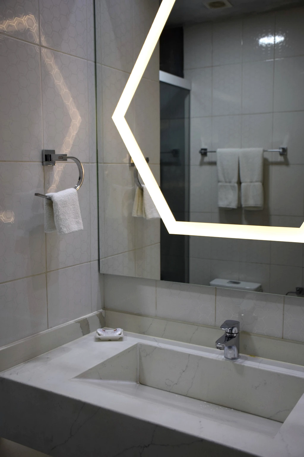 Stone bathroom with an illuminated geometric mirror and white basin