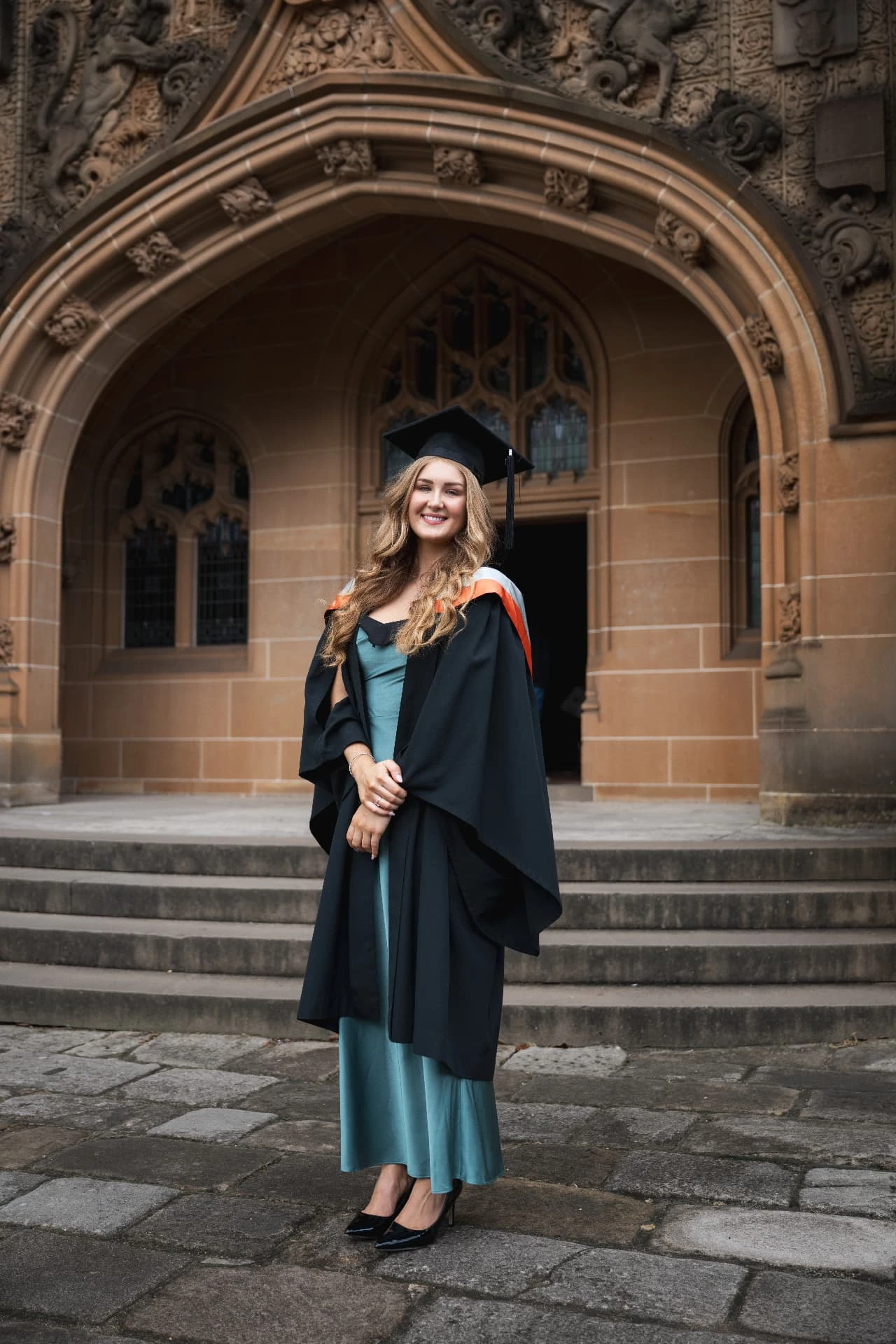A graduate in an academic gown beneath an ornate stone archway
