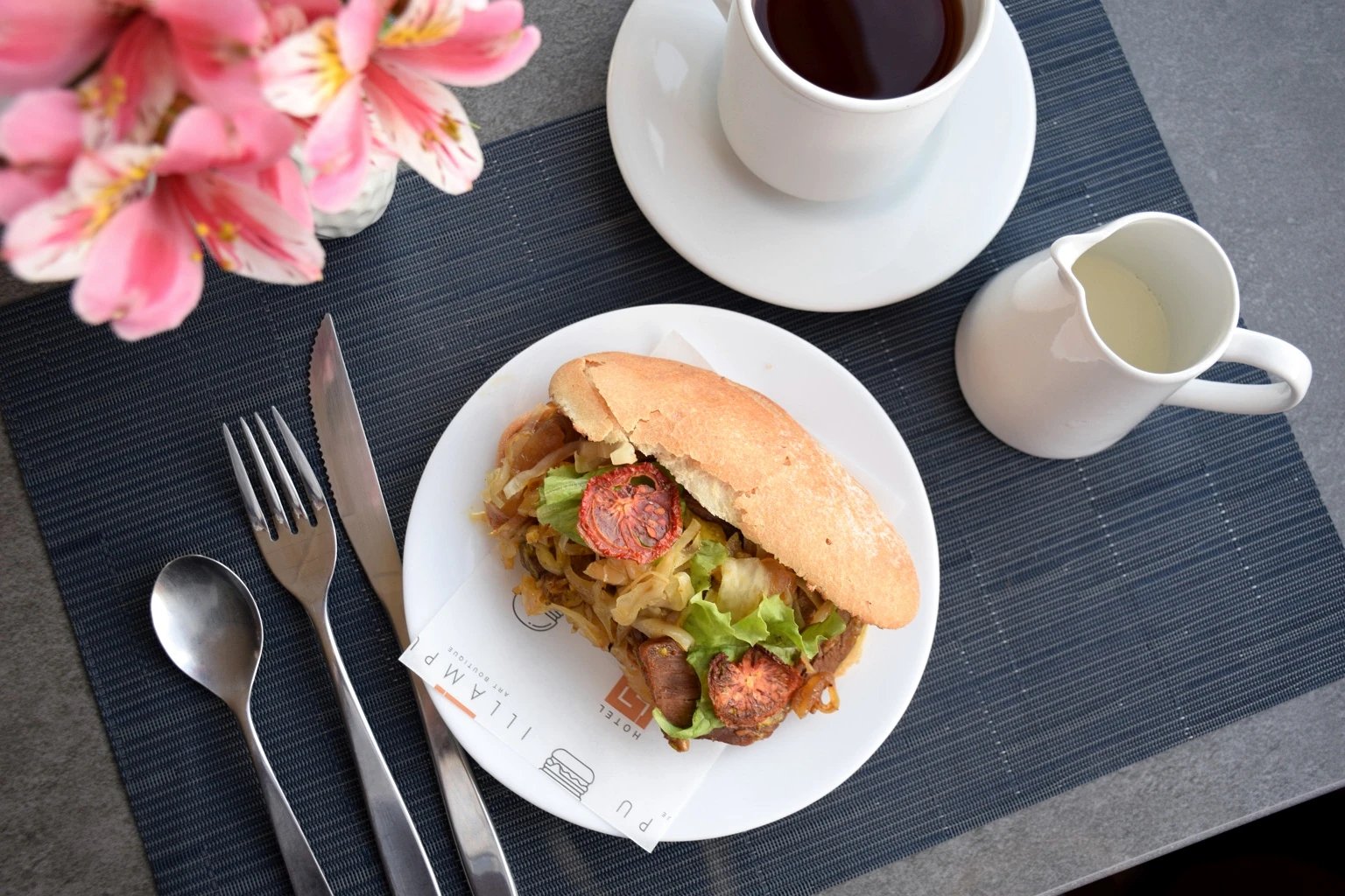 Overhead view of breakfast, coffee and pink flowers on a dark table