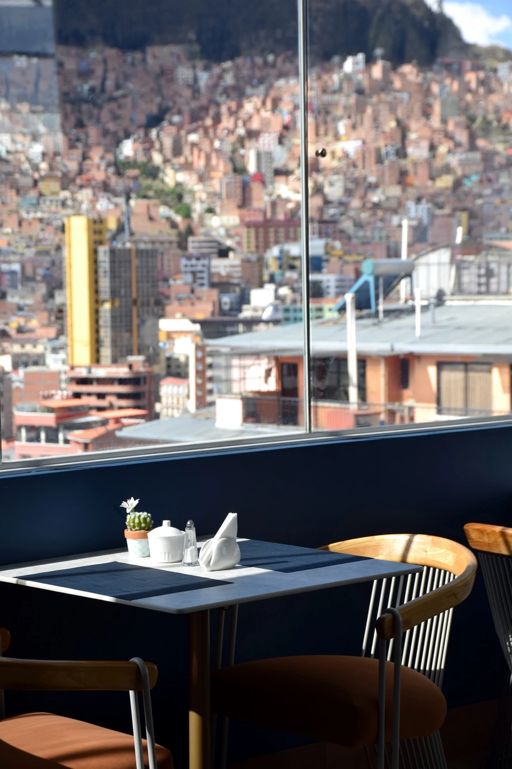 A dining table beside a window overlooking a densely built hillside city