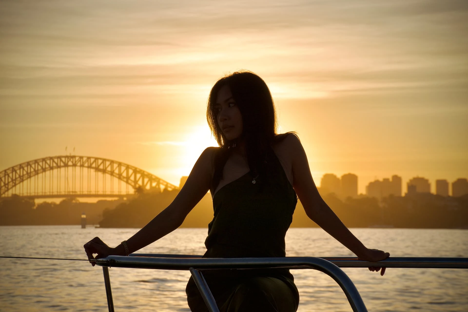 Silhouette at a waterfront railing with a harbour bridge against golden evening light