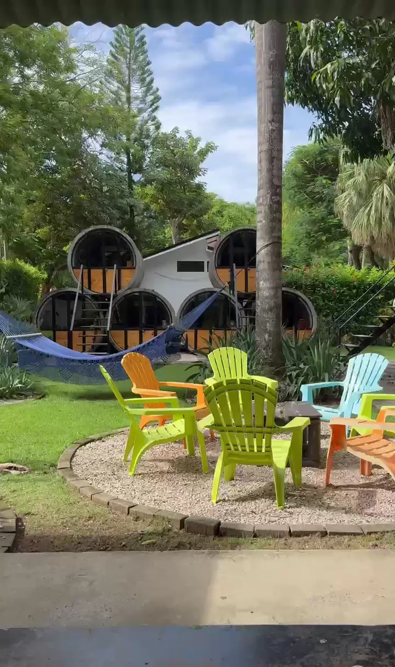 A garden courtyard of timber sleeping cabins, colourful lawn chairs and a hammock