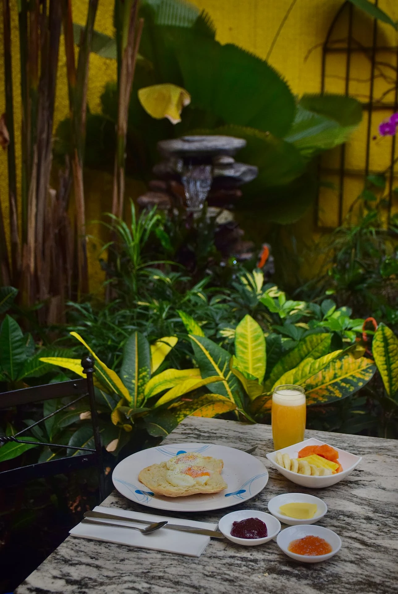 Breakfast and orange juice served beside lush tropical plants and a fountain