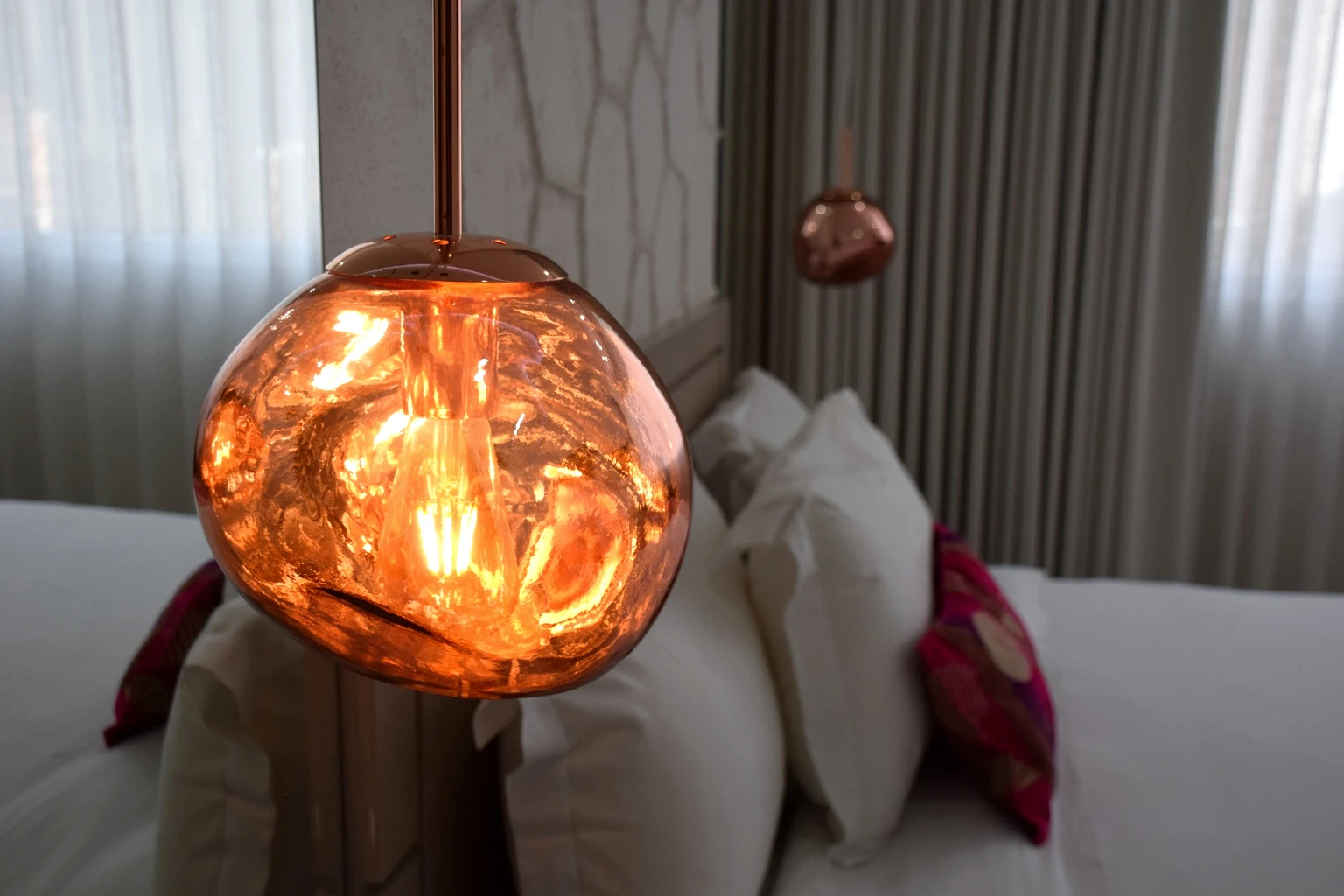 Warm copper pendant light beside a bed with colourful cushions